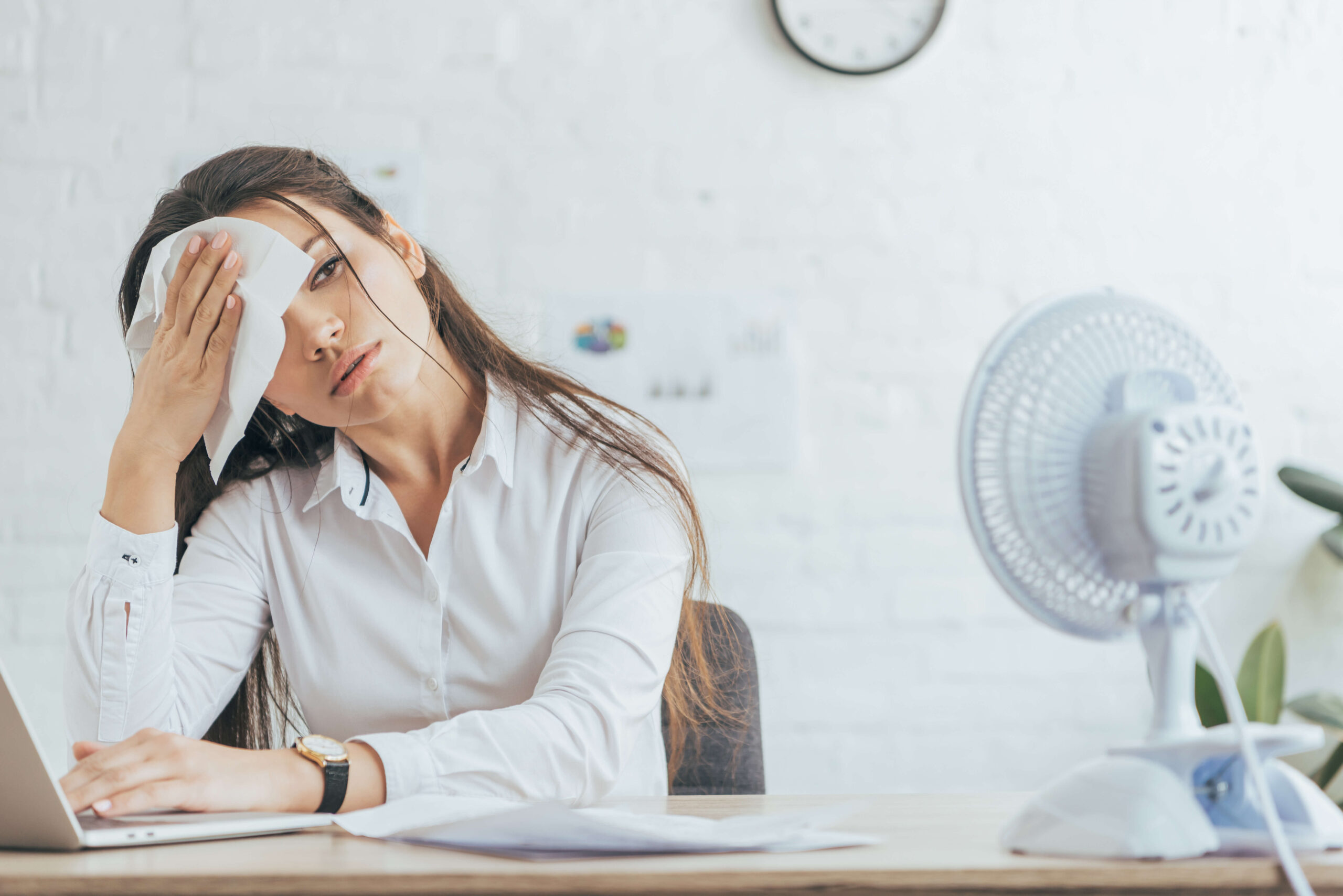 Woman wiping her forehead with napkin in front of fan